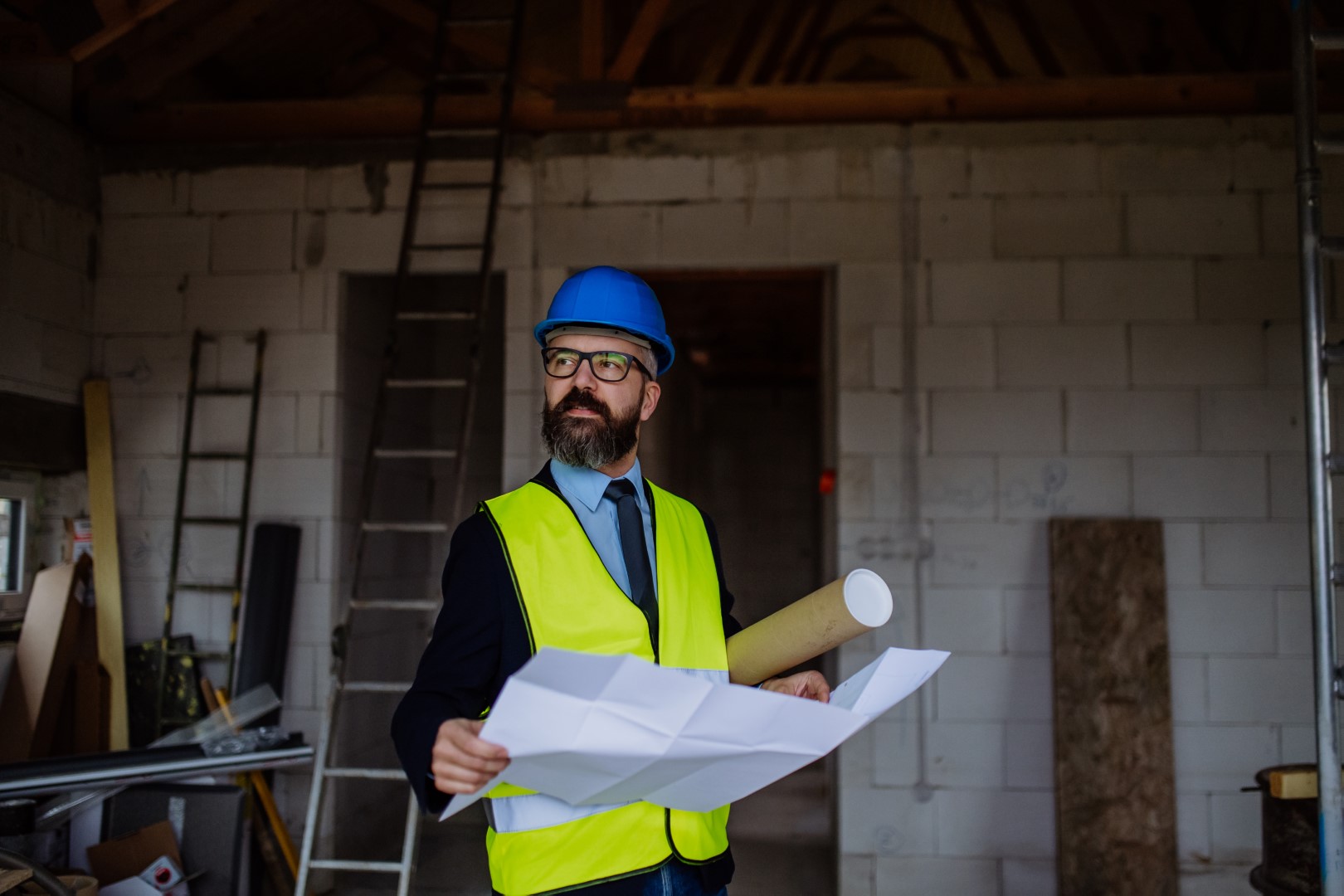 Mature businessman controlling blueprints from unfinished house.